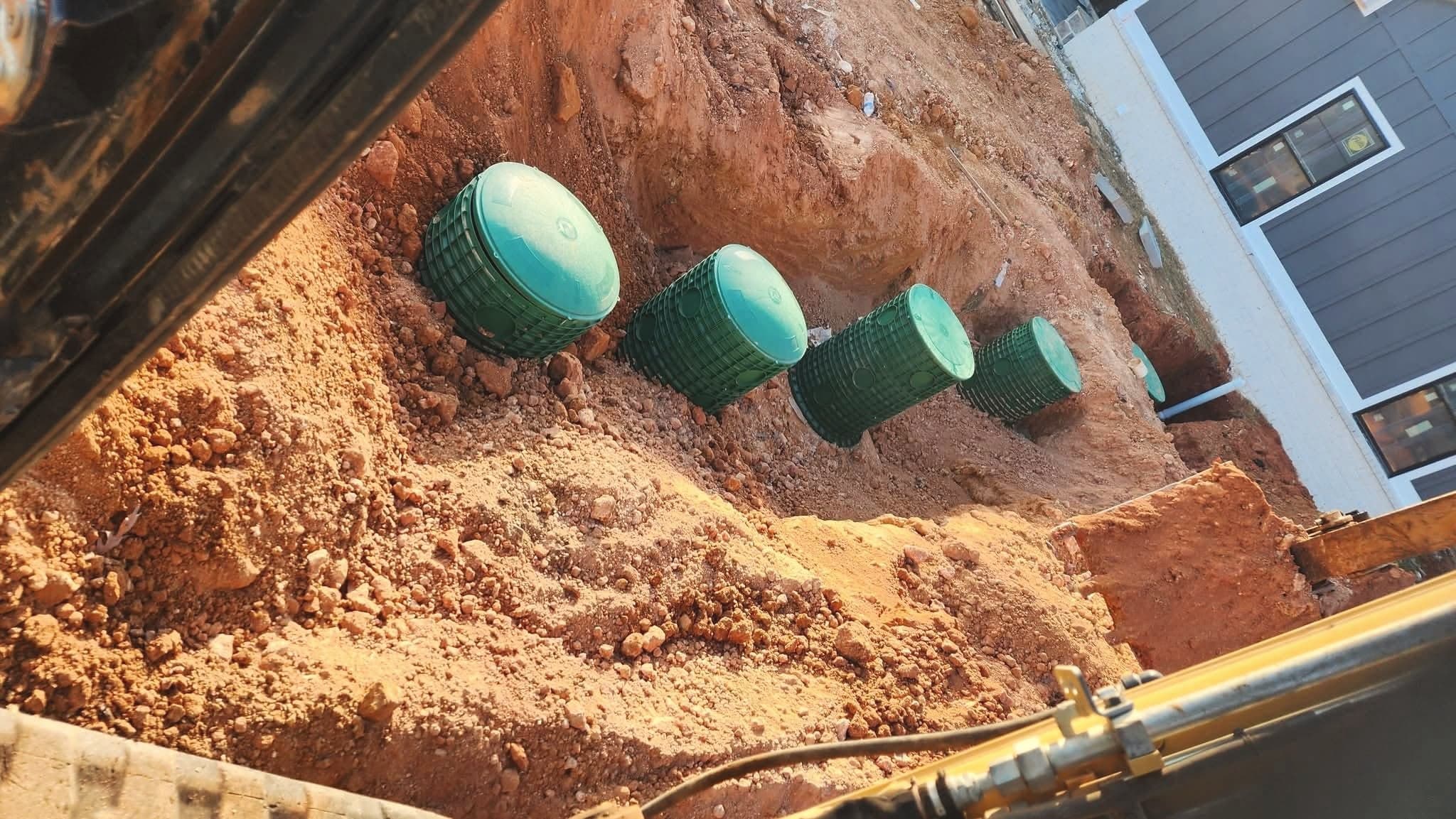 From our job files: a row of green septic riser lids in a fresh excavation beside a new home, seen from the excavator cab